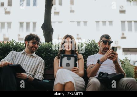 Business colleagues working outdoors on a sunny day, using digital devices on a bench Stock Photo