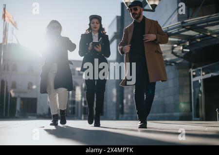 Three young business entrepreneurs walking and working with their smart phones in a sunny urban environment, illustrating remote collaboration. Stock Photo
