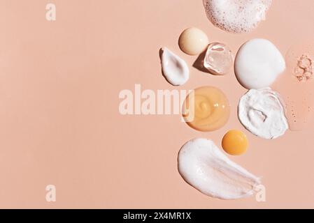 Set of sample cosmetic on beige pink background, copy space. Beauty or skin care products swatches: moisturizer, serum essence, cleanser foam, tonic, Stock Photo