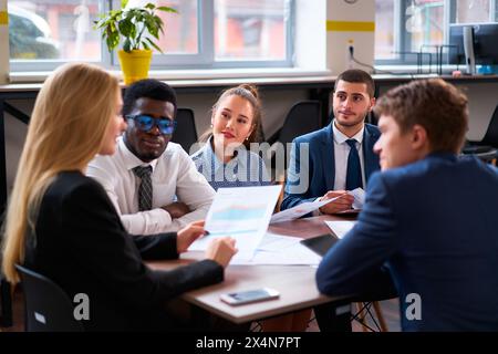 Multiethnic corporate team in meeting room discuss strategy. Diverse group of businesspeople with charts engage in brainstorming, collaboration. A Stock Photo