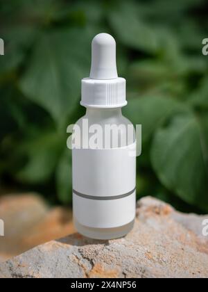 Mock up glass dropper bottle with white empty label on a rock with blurred leaves in the background. Selective focus. Cosmetic pipette in nature Stock Photo