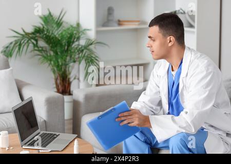 Young doctor video chatting with patient on laptop at home Stock Photo