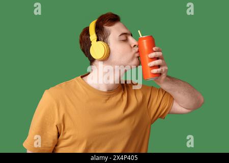 Young man in headphones kissing can of soda on green background Stock Photo