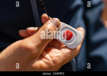 old hand holding an SOS button, highlighting its use for emergencies with focus on the red button Stock Photo