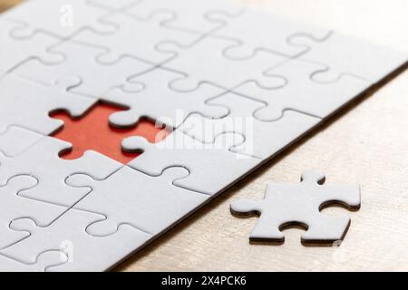 Blank puzzle with one missing piece next to the whole with a red placer where the last piece belongs. Concept for problem solving. Stock Photo