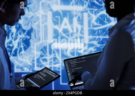 Hardworking colleagues write code on tablet and laptop to visualize artificial intelligence neural networks using augmented reality. Teamworking coworkers run AI script for information processing Stock Photo