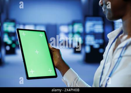 Experienced developer in server room uses green screen tablet to future proof network from downtimes and unexpected system failures. IT specialist with mockup device ensures increased data security Stock Photo