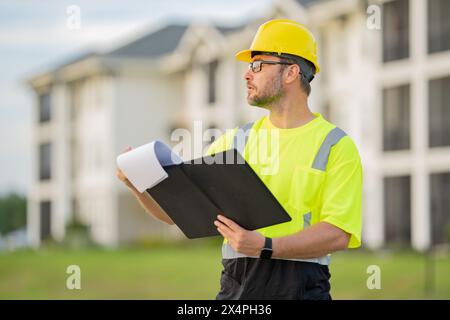 Engineer with clipboard, building inspection. Caucasian man, construction worker in helmet at construction site. Engineer worker in hardhat near new h Stock Photo