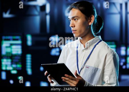 IT consultant with tablet between server hub clusters providing processing resources for businesses worldwide. Diligent worker fixes data center mainframes tasked with managing massive databases Stock Photo
