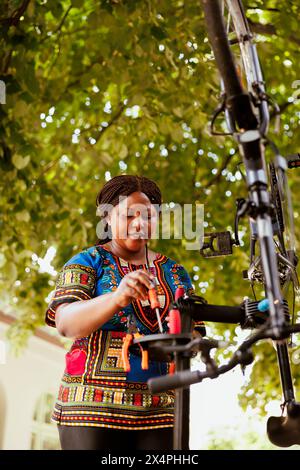 Sports-loving black woman holding professional equipment for bike maintenance in home yard. Determined african american individual focuses on repairing bicycle with specialized tools Stock Photo