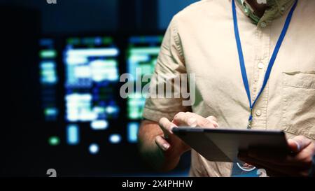 Serviceman doing system analysis, typing data on tablet of needed adjustments in supercomputers server hub housing advanced data storage infrastructure supporting critical IT workloads, close up Stock Photo
