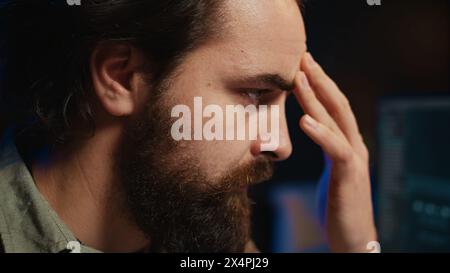 Stressed programmer updating artificial intelligence neural networks, writing binary code scripts. Freelancing system administrator upgrading high tech AI, confused by complexity, camera B close up Stock Photo