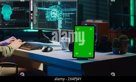Focus on isolated screen tablet next to programmer updating artificial intelligence, making it become sentient. IT specialist programming self aware AI with chroma key device, camera A Stock Photo