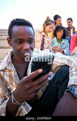 Serious black guy using smart phone. African American man holding cell outdoor with friends Stock Photo