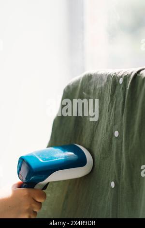 Woman Using Handheld Steamer on a Green Garment at Home During Daytime Stock Photo