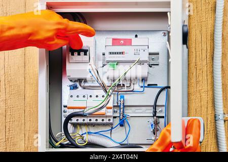 An electrician wearing protective dielectric gloves turns off power supply to circuit breaker in an external electrical panel. Stock Photo
