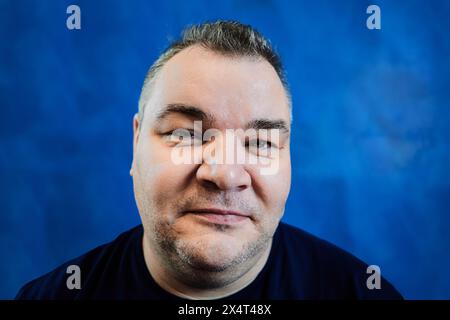 Sly face of Caucasian man 47 years old closeup on blue background. Stock Photo