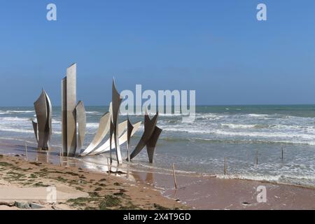 View of monument on Omaha beach. Waves rolling in from the ocean. Blue sky and no visible people. Stock Photo