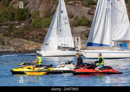 Stenungsund, Sweden - August 21 2021: Three persons on water scooters lying still in the water. Sailboats in background. Stock Photo