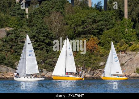 Stenungsund, Sweden - August 21 2021: Three sailboats on sunny day at sea. Crew visible on the boats. Rural rocky background with trees. Stock Photo