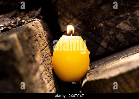 A burning candle in the shape of a yellow chicken egg stands on old wooden boards on the street, Easter holiday Stock Photo