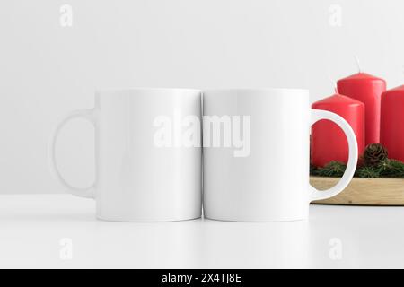 Two white mugs mockup with candles on a table. Christmas decoration Stock Photo