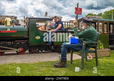 A volunteer drives The Railway Mission minature steam locomotive past a guard  at South Downs Light Railway, Pulborough, UK Stock Photo