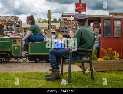 A volunteer drives The Railway Mission minature steam locomotive and its passengers passed a volunteer guard South Downs Light Railway, Pulborough, UK Stock Photo