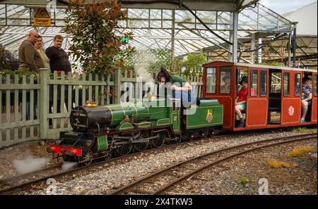 A volunteer drives The Railway Mission minature steam locomotive and its carriages at South Downs Light Railway, Pulborough, UK Stock Photo