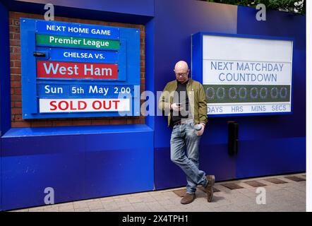 A fan stands by to the next fixture board outside the ground ahead of the Premier League match at Stamford Bridge, London. Picture date: Sunday May 5, 2024. Stock Photo