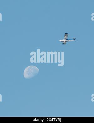Airplane flies near moon against clear blue sky Stock Photo