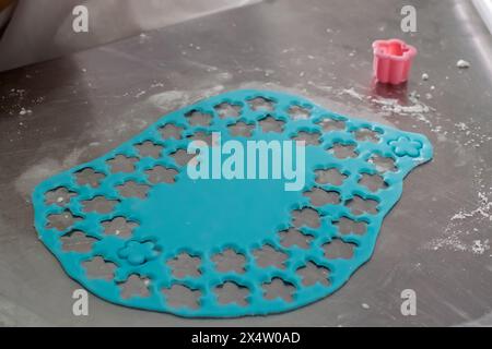 A blue sheet of paper with flower shapes cut out on it. The paper is on a table with a pink object in the background Stock Photo