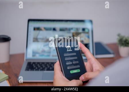 A person is using a cell phone to pay for something on a laptop. The person is holding the phone in front of the laptop, and the screen of the phone i Stock Photo