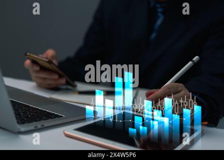 A business analysis examines interactive data charts on a tablet while simultaneously using a smartphone. Stock Photo