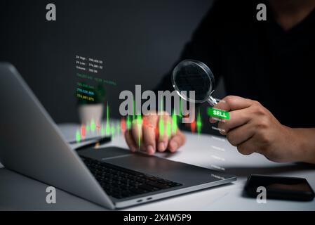 A person examines stock market indicators on a laptop screen using a magnifying glass. The focus on specific data points suggests a detailed analysis Stock Photo