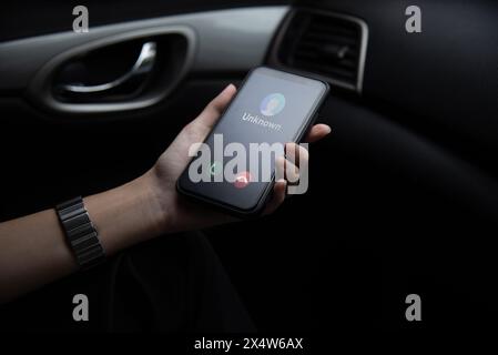 Hand holding a smartphone displaying an unknown caller ID Scam, fraud or phishing with smartphone inside a vehicle. Stock Photo