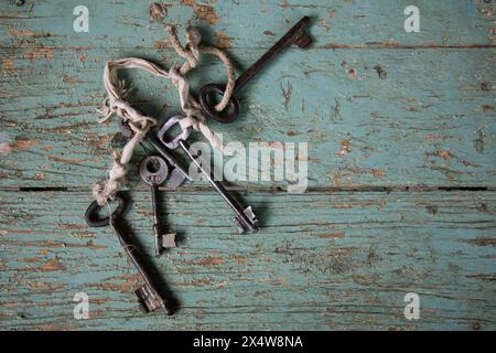 Collection of antique iron keys tied with string on distressed turquoise wooden boards, rustic texture and vintage detail. Stock Photo