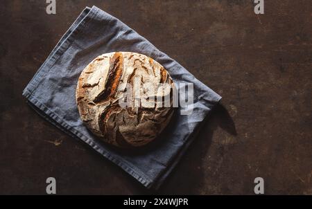 Artisan sourdough bread on a blue linen napkin set against a textured dark brown backdrop Stock Photo