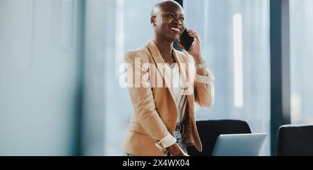 Successful African businesswoman in her office, using a smartphone and discussing business on the phone. She is professional and focused. Stock Photo