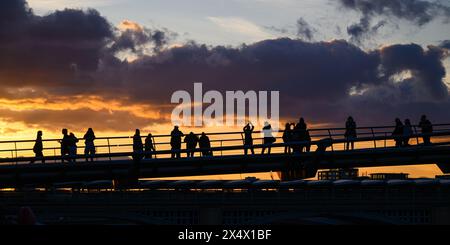 Silhouettes of people on Millennium Bridge watching orange sunset on clouds in central London Stock Photo