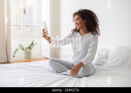 Woman Sitting on Bed Taking Selfie With Phone Stock Photo