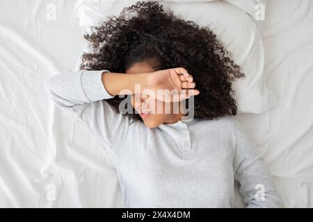 Young Woman Awakening and Shielding Her Eyes From Morning Light Stock Photo