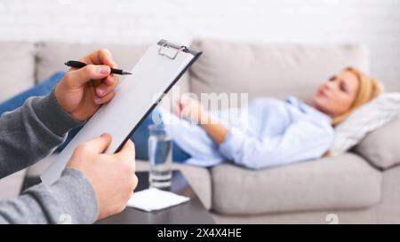 Psychologist listening to depressed patient and writing down notes Stock Photo