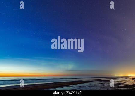 Starry night sky after sunset with weak Aurora Borealis northen lights on the Baltic Sea beach in Latvia at May Stock Photo