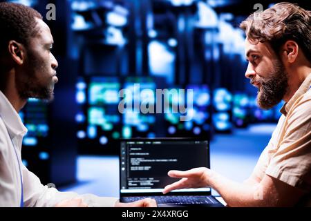 Adept IT developers colleagues writing script code in server hub on laptop terminal. Experienced programmer team doing maintenance work in cloud computing computer business updating racks software Stock Photo