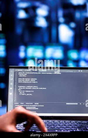 Computer scientists updating rackmounts, writing lines of code on laptop terminal, close up. Employees using JavaScript, Java, and database programming to ensure seamless server farm computing Stock Photo