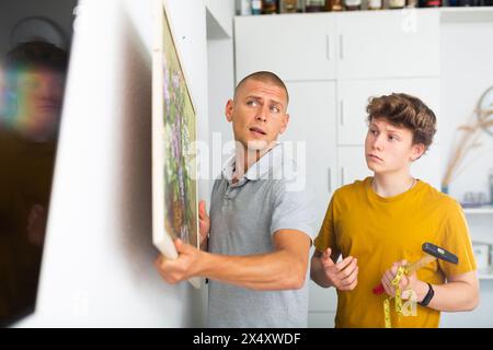 Son helps father to hang the painting on the wall of house Stock Photo