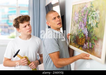 Son helps father to hang the painting on the wall of house Stock Photo