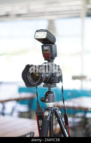 Black Canon DSLR camera mounted on a tripod with an external flash ready to use Stock Photo