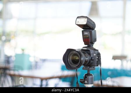 Black Canon DSLR camera mounted on a tripod with an external flash ready to use Stock Photo